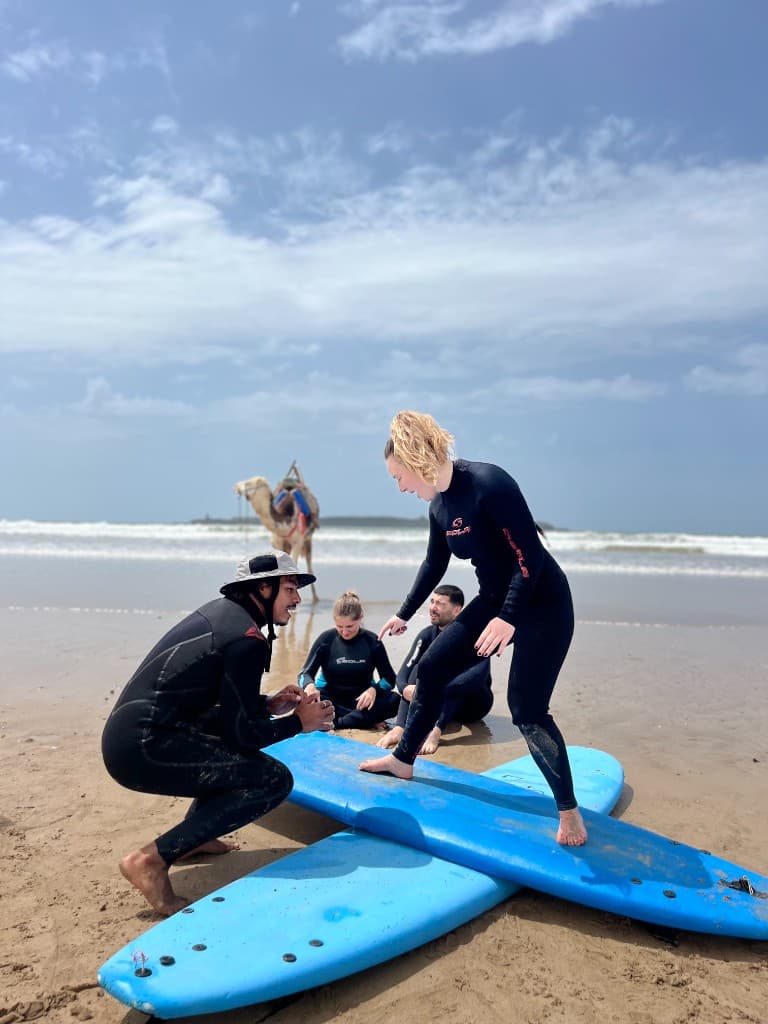 Moniteur de surf certifié IKO enseignant la position sur la plage d'Essaouira, Maroc, avec des élèves et l'océan en arrière-plan