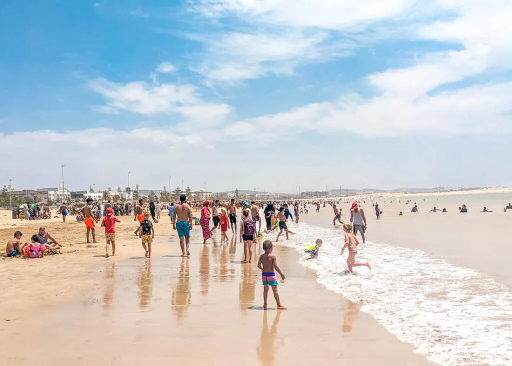 Busy summer day on Essaouira beach — surf lessons and families in the bay